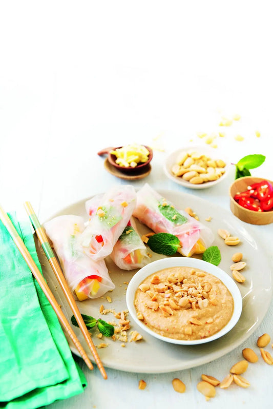 Frische vietnamesische Sommerrollen, gefüllt mit Gemüse, Kräutern und Reisnudeln, serviert mit cremigem Erdnuss-Dip in einer kleinen Schale.