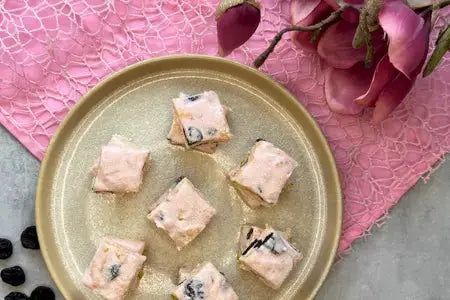 In Stücke geschnittenes pinkes Crisp Nougat mit Crackern, Nüssen und Trockenfrüchten auf einem Teller.