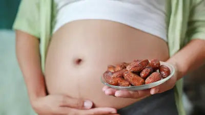 Schwangere Frau hält eine Schale mit Datteln vor ihrem runden Babybauch