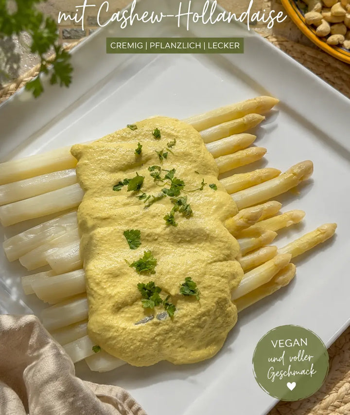 Weißer SPargel auf einem Teller mit gelber Cashew-Soße und grünen Kräutern.