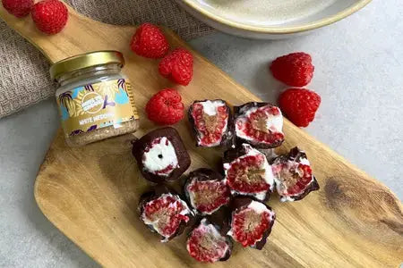 Schokoladenüberzogene gefrorene Himbeeren mit cremigem Nussmus‑Kern, serviert als kleiner Snack auf einem Brett.