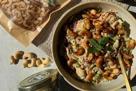 Bunter Quinoa‑Salat mit Edamame, Karotten, Gurke, Zuckerschoten, Kräutern und knusprigen Chili‑Cashews in einer Schüssel.