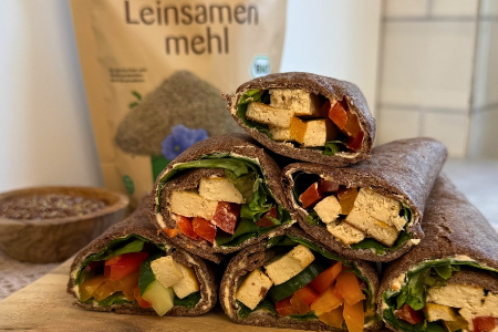 Vegane Leinsamenwraps mit würzigem Tofu, frischem Salat, Gurken und bunten Paprikastreifen, dekorativ aufgeschnitten und gestapelt serviert.