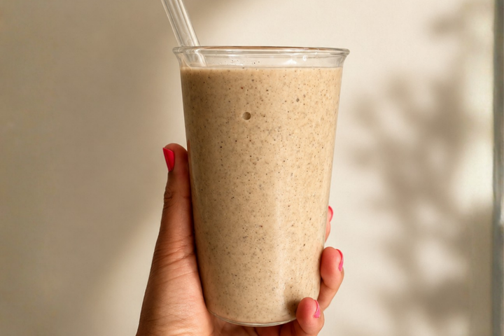 Cremiger Smoothie in einem Glas, gehalten von einer Hand, vor einem warm beleuchteten Hintergrund.