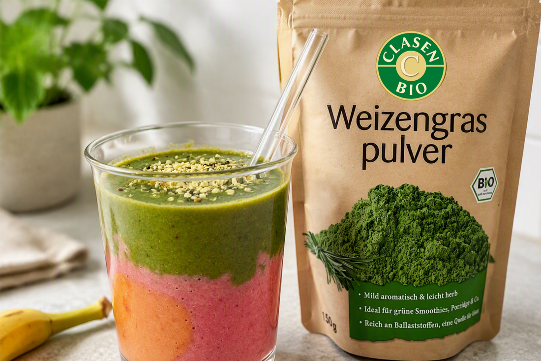 Grüner Weizengras-Smoothie mit pinker Fruchtschicht und Hanfsamen-Topping in einem Glas, daneben eine Packung Bio-Weizengraspulver.