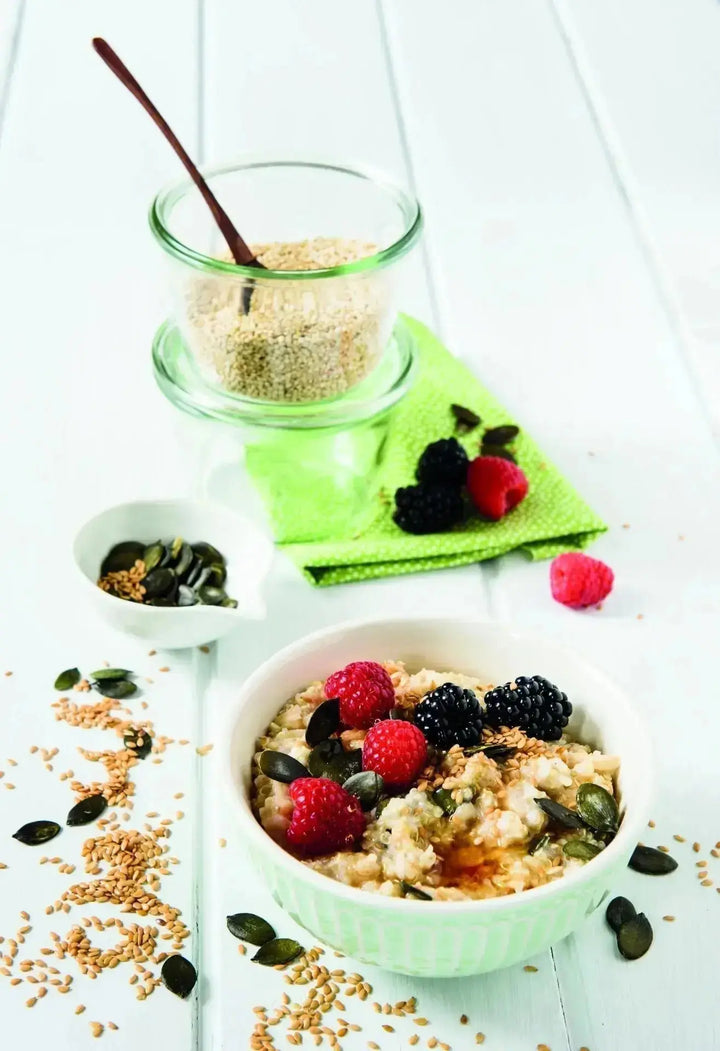 Bircher Quinoa mit Kürbiskernen, Goldleinsamen und Beeren, serviert in einer Schale, garniert mit Nüssen, Samen und frischen Beeren