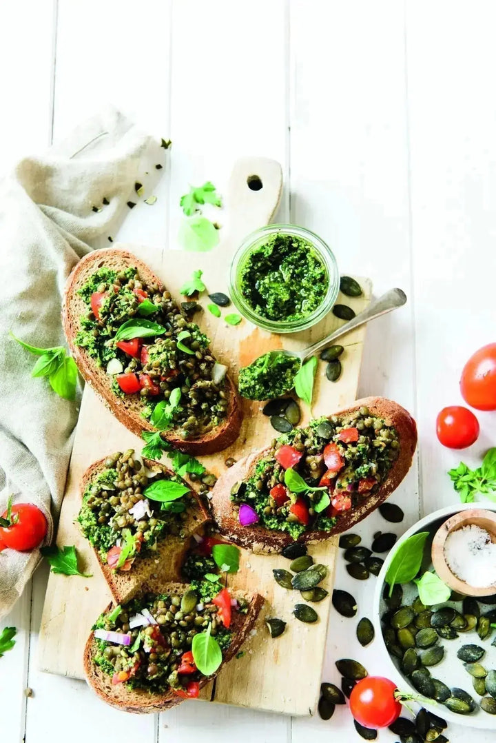 Bruschetta mit würzigem Kürbiskern-Pesto und grünen Linsen, serviert auf knusprigem Brot auf einem Holzbrett, daneben Kürbiskerne als Dekoration