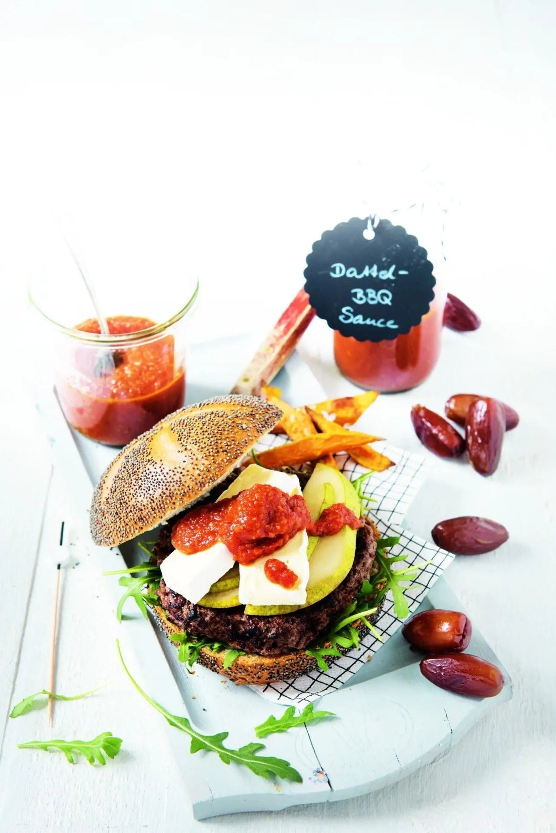 Burger mit Dattel-BBQ-Sauce, serviert in einem Brötchen mit Salat und Gemüse, daneben etwas Sauce als Dip