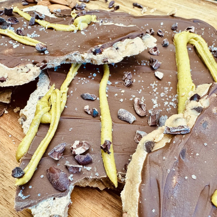 Cookie Dough Bars mit Mandelprotein und Kakaonibs, serviert auf einem Teller, garniert mit Salz und Pistaziencreme, Kakaonibs sichtbar auf der Oberfläche