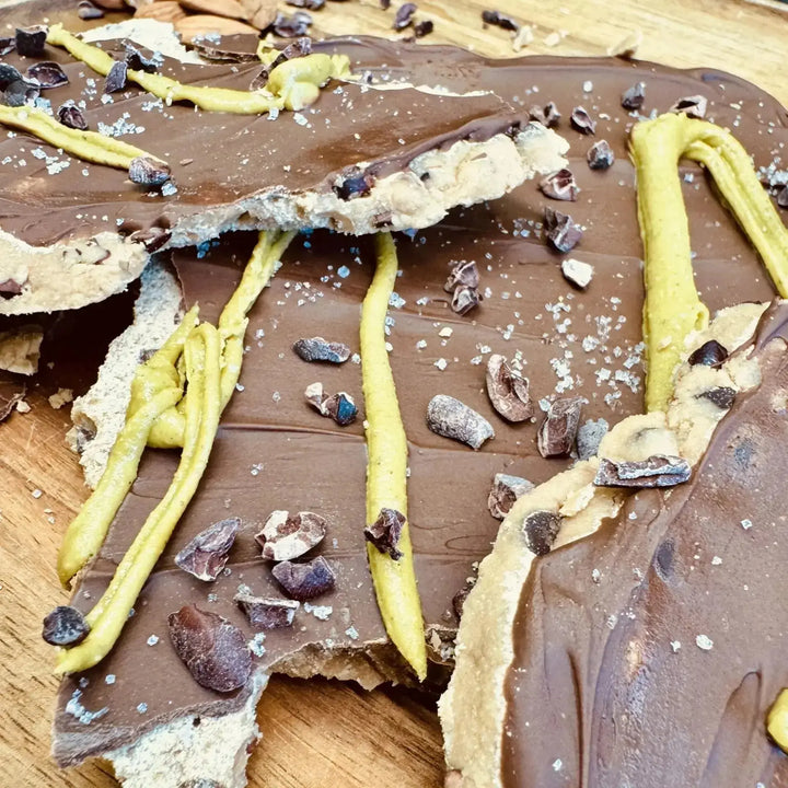 Cookie Dough Bars mit Mandelprotein und Kakaonibs, serviert auf einem Teller, garniert mit Salz und Pistaziencreme, Kakaonibs sichtbar auf der Oberfläche