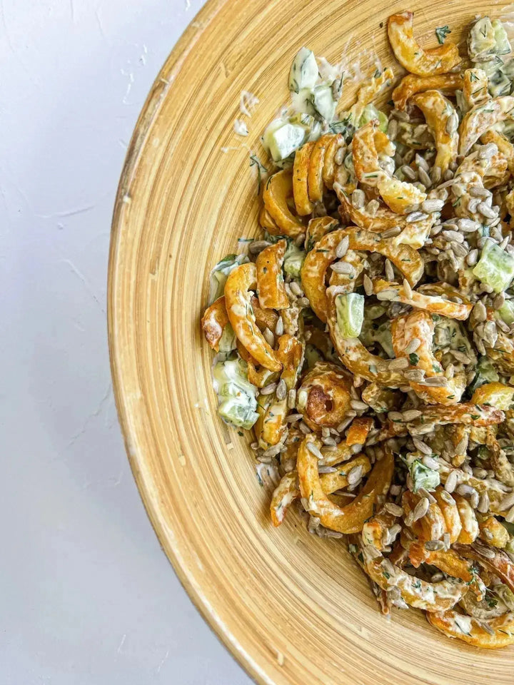 Curly-Fries Salat mit Sonnenblumenkernen, serviert auf einem Teller mit knusprigen Pommes