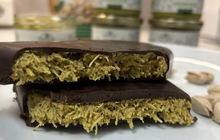 Aufgeschnittene Schokolade mit orientalischer Füllung aus Pistazien und Kadaifi, inspiriert von Aromen aus Dubai. Im Hintergrund liegen Pistazien.