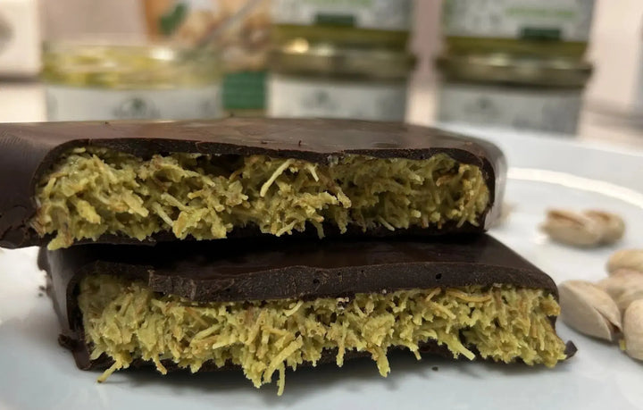 Aufgeschnittene Schokolade mit orientalischer Füllung aus Pistazien und Kadaifi, inspiriert von Aromen aus Dubai. Im Hintergrund liegen Pistazien.