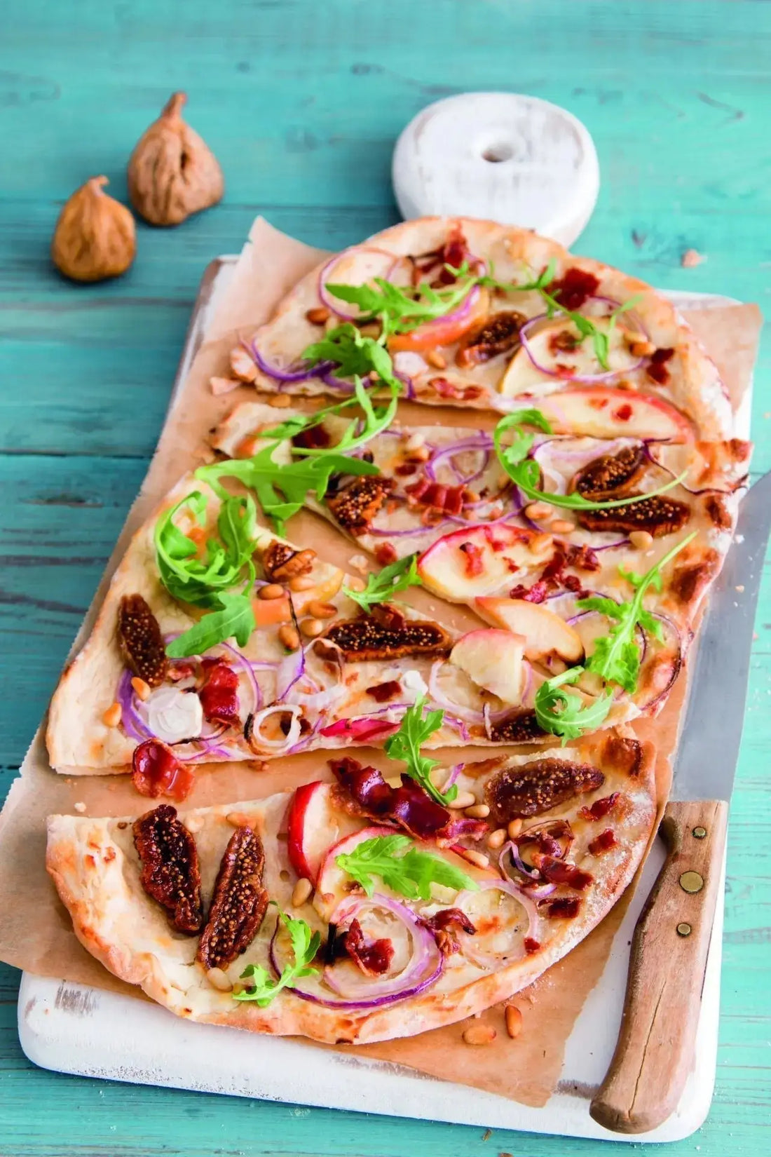 Flammkuchen mit frischen Feigen, Ziegenfrischkäse und knusprigen Baconchips, goldbraun gebacken und angerichtet auf einem Holzbrett