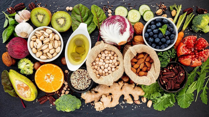 Vielfältiges, frisches Gemüse, Obst, Nüsse von oben fotografiert – darunter Brokkoli, Orange, Avocado, Kiwi, Pistazien, Gurke und mehr, bunt arrangiert.