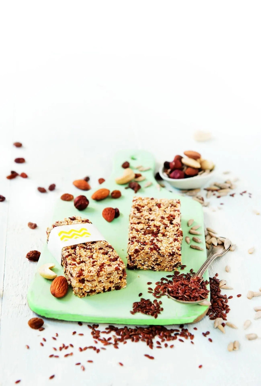 Frühstücksriegel mit Saaten und Studentenfutter, daneben Nüsse, Trockenfrüchte und Samen als Dekoration