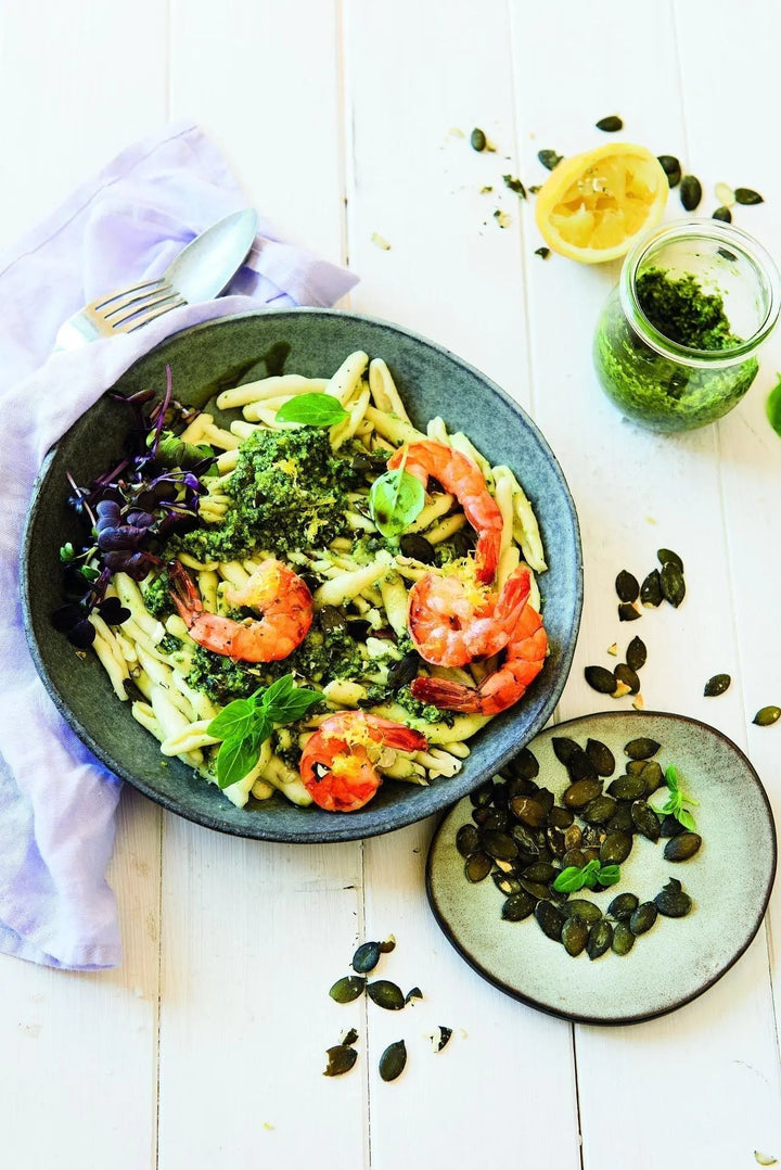 Garnelen-Pasta mit Kürbiskern-Bergkäse-Pesto, angerichtet auf einem Teller mit sichtbaren Garnelen und grünem Pesto“
