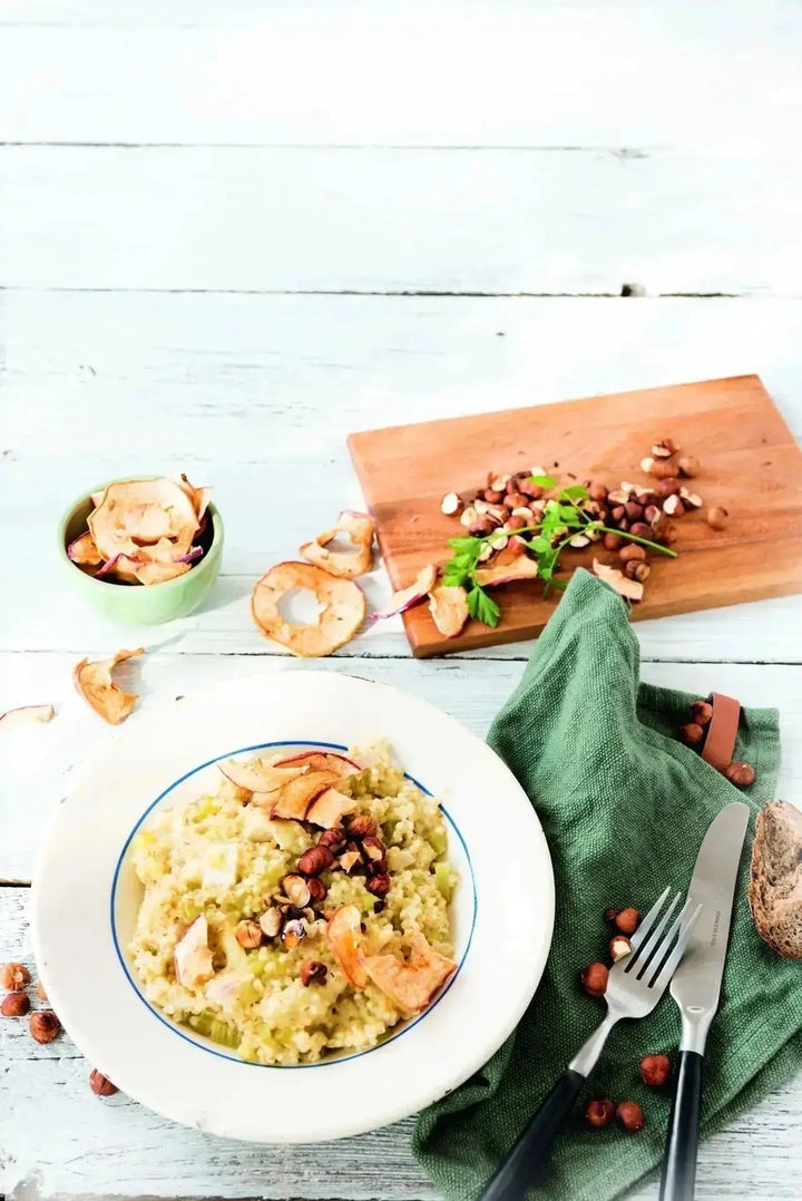 Graupen-Risotto mit geschmolzenem Brie, knusprigen Apfelchips und gerösteten Haselnusskernen, cremig angerichtet auf einem Teller