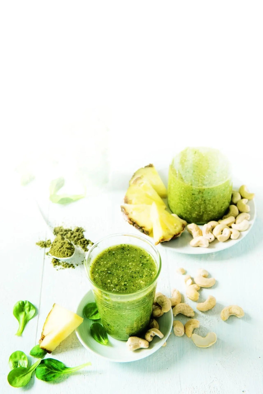 Grüner Smoothie mit Cashewkernen und Hanfproteinpulver in einem Glas, garniert mit Minze, daneben Cashewkerne und ein Löffel Hanfproteinpulver