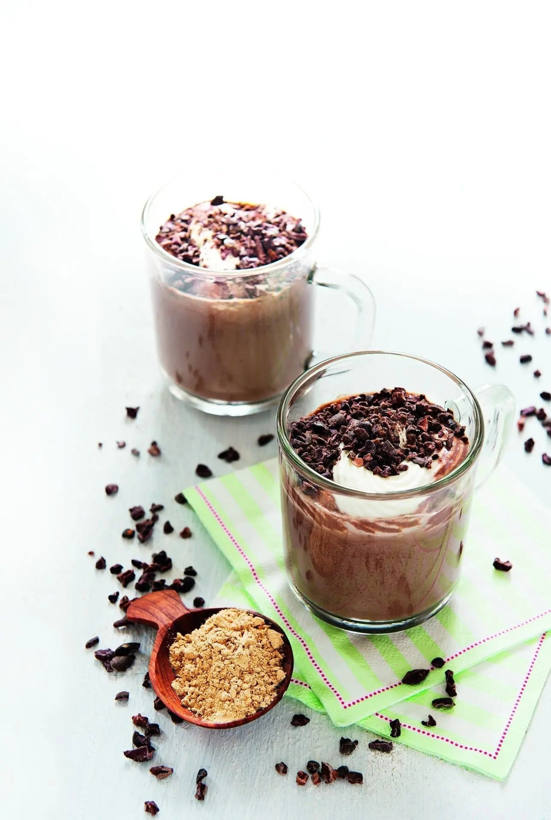 Zwei Gläser Happy Chocolate mit Macapulver, daneben ein Löffel Macapulver und Kakaonibs