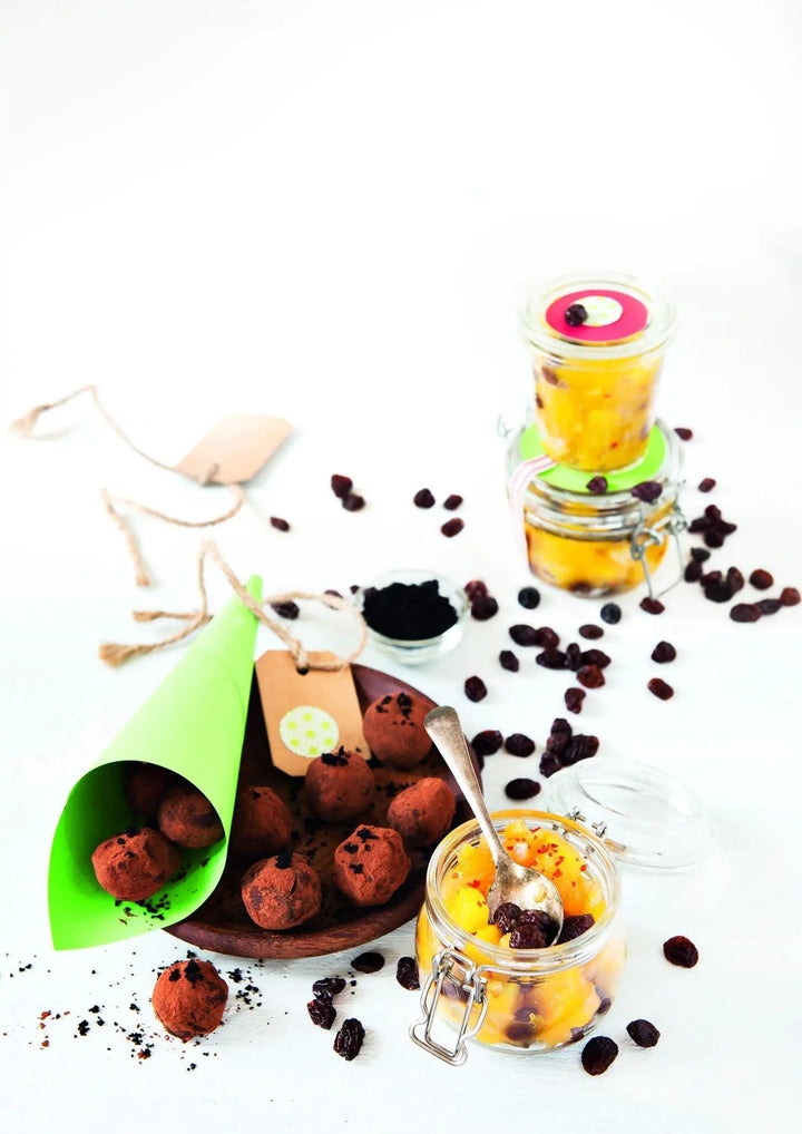 Schokoladen-Trüffel mit Açaipulver, daneben Gläser mit Ingwer-Mango-Chutney und Açaipüree, dekorativ angerichtet