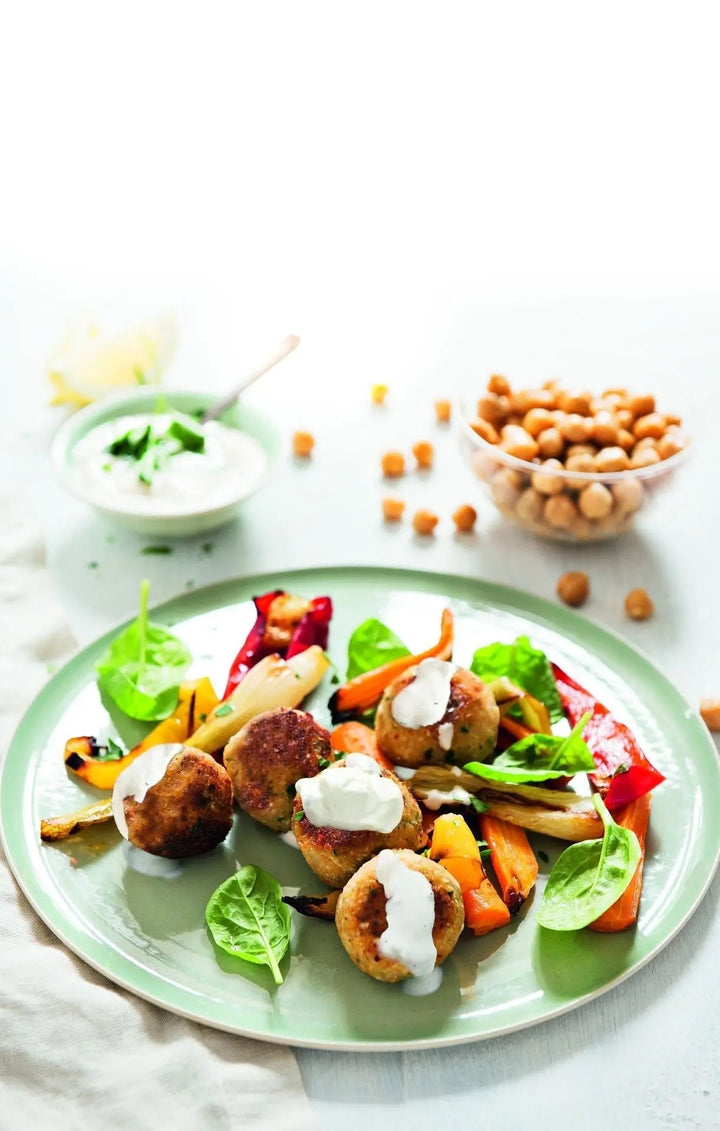 Kichererbsen-Blumenkohl-Bällchen mit buntem Gemüse und Tahin-Dip, angerichtet auf einem Teller, mit frischem Gemüse farbenfroh dekoriert