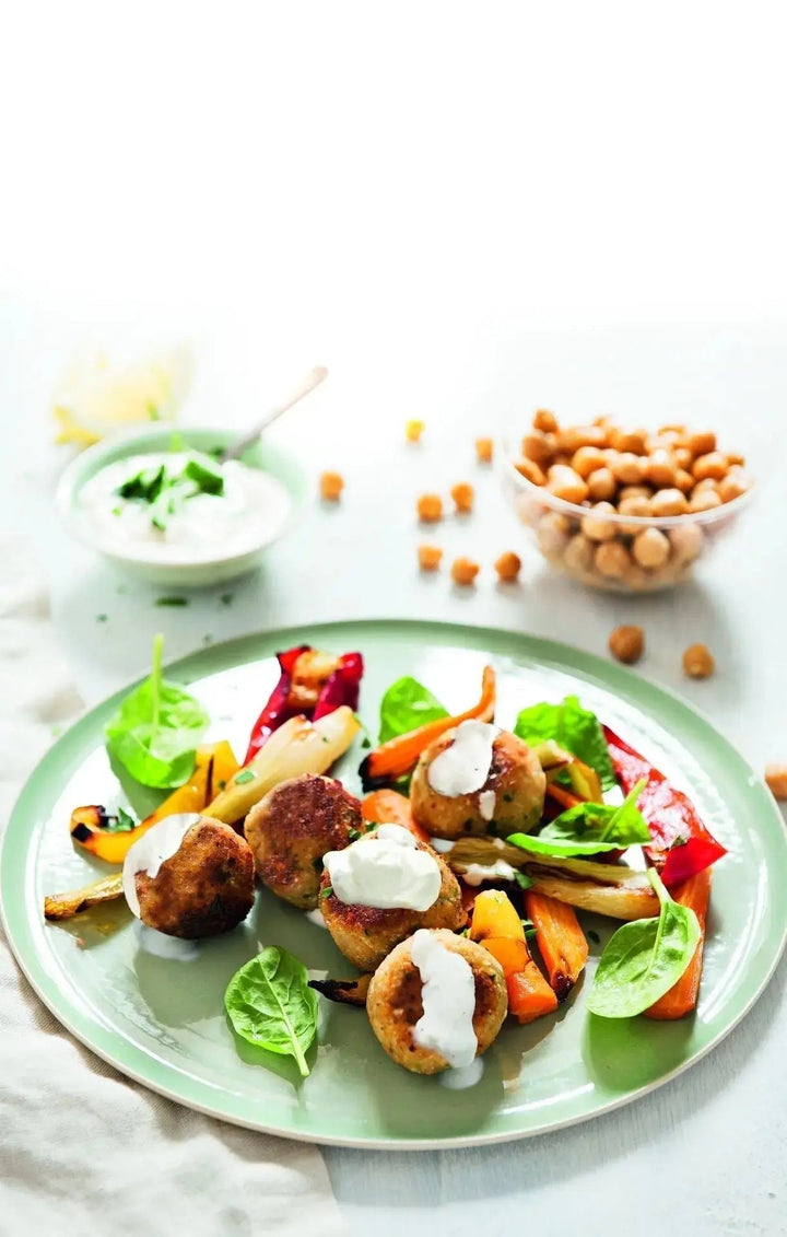 Kichererbsen-Blumenkohl-Bällchen mit buntem Gemüse und Tahin-Dip, angerichtet auf einem Teller, mit frischem Gemüse farbenfroh dekoriert