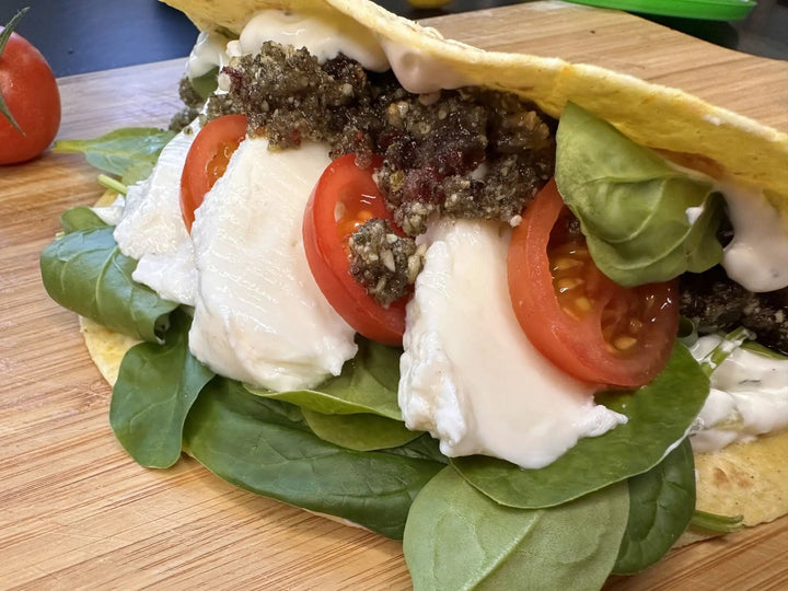 Kürbis-Cranberry-Pesto serviert auf einer Tortilla mit frischen Tomaten, Spinat und Büffelmozzarella, farbenfroh angerichtet