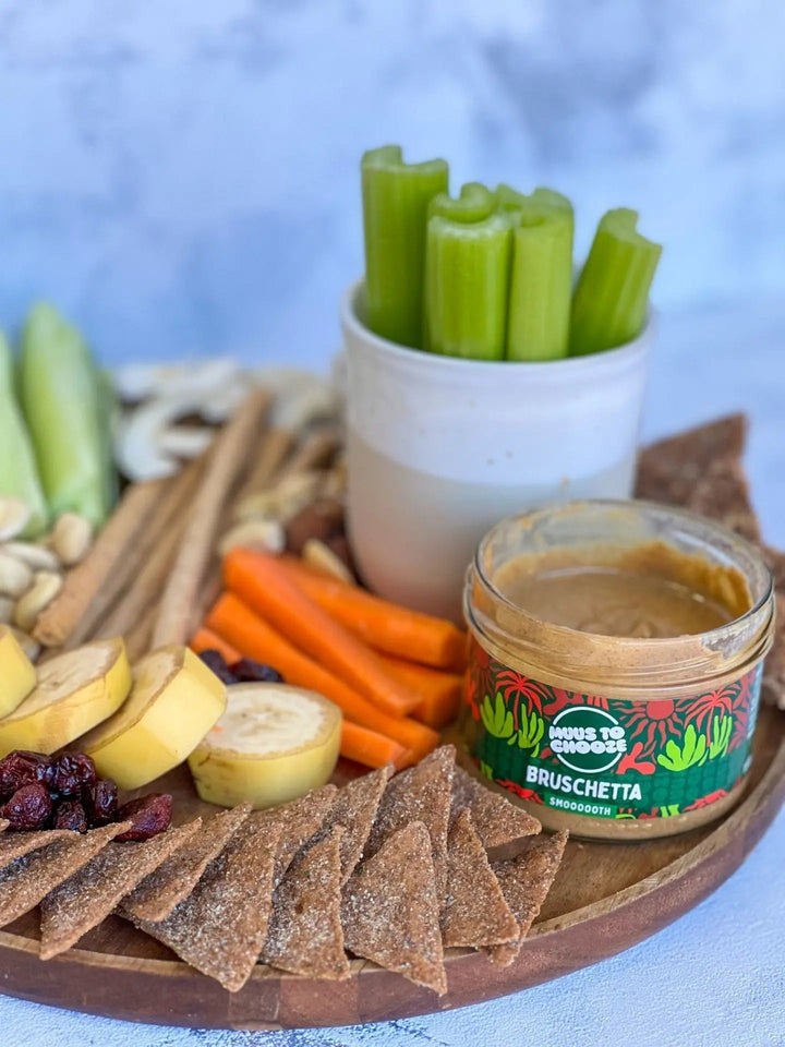 Clasen Bio Snackplatte auf Holzbrett mit Gemüse, Trockenfrüchten, Crackern, Nüssen und einem Glas Bruschetta-Nussmus als Dip in der Mitte