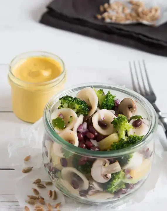 Pasta-Salat mit Azukibohnen in einem Glas serviert, daneben ein Schälchen mit Curry-Dressing
