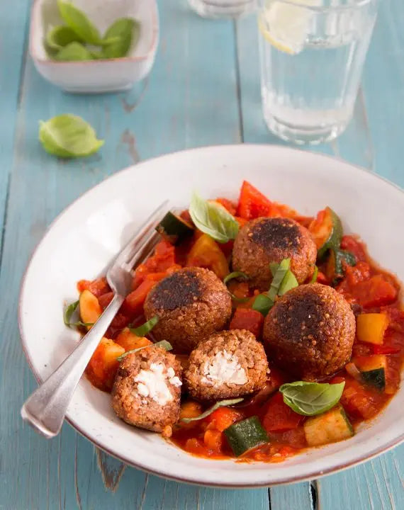 Quinoa-Feta-Bällchen auf Paprika-Zucchini-Sugo, serviert auf einem Teller mit bunter Gemüsesauce