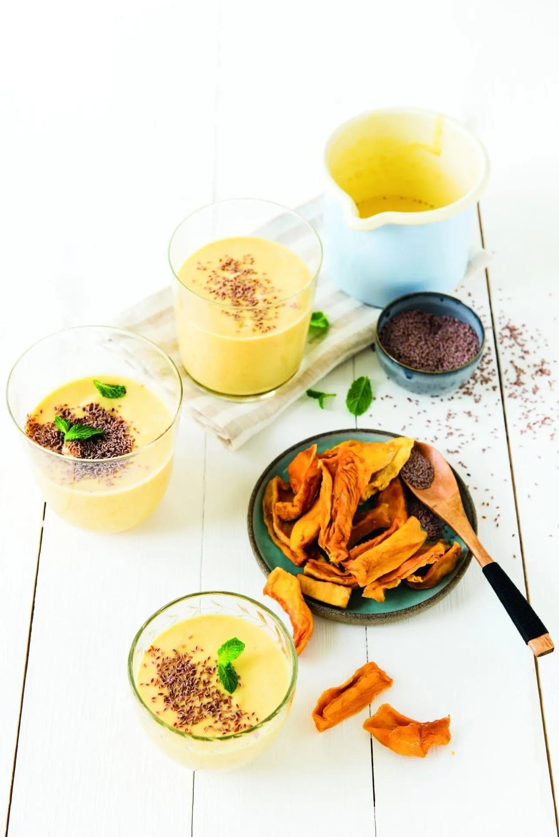 Leichter Mango-Lassi mit Macapulver und Flohsamen, serviert in einem Glas, garniert mit Mangostückchen und einem Löffel Macapulver