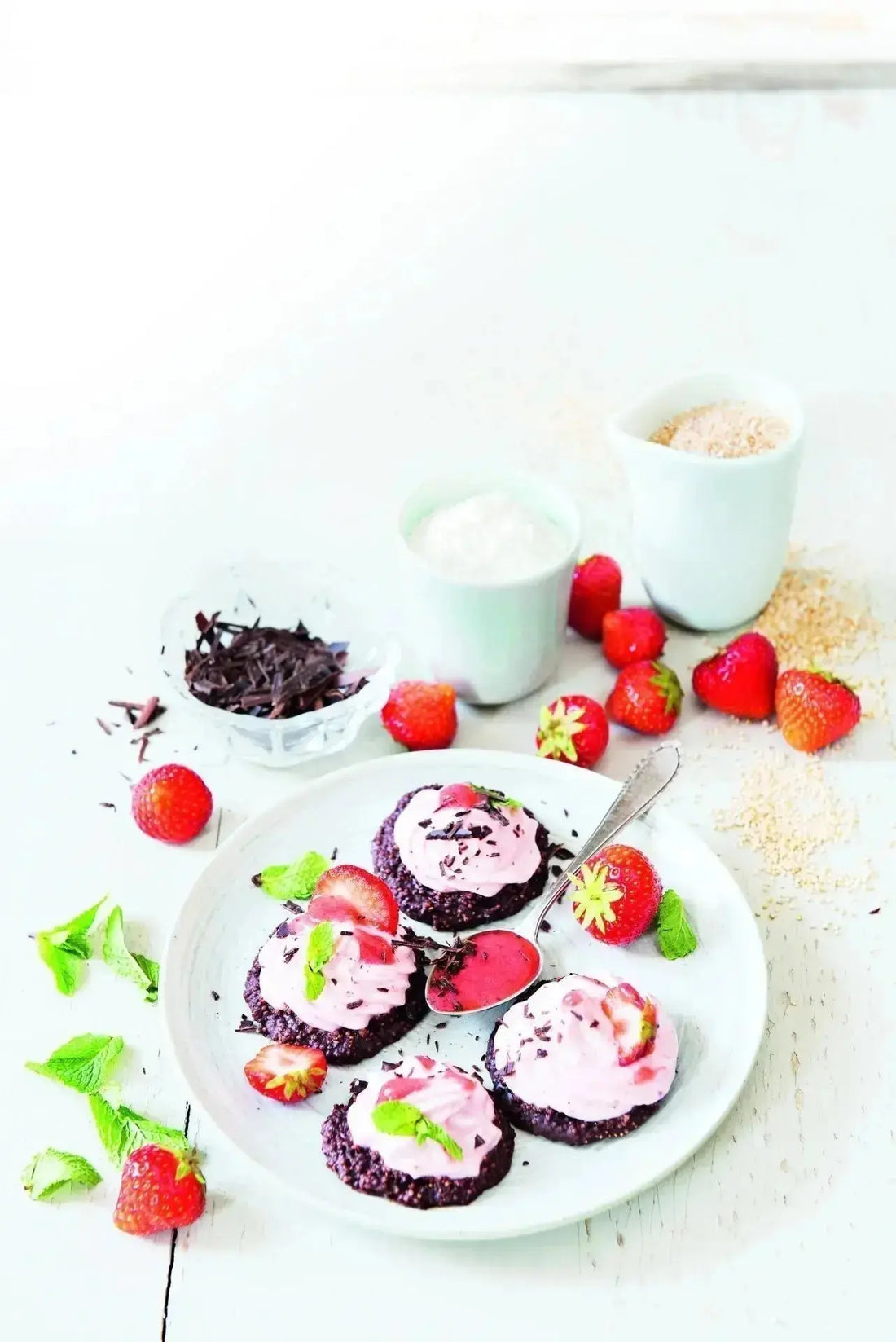 Schoko-Kokos-Taler mit Erdbeercreme auf einem weißen Teller, garniert mit frischen Erdbeeren, Kakaonibs und Minzblättern