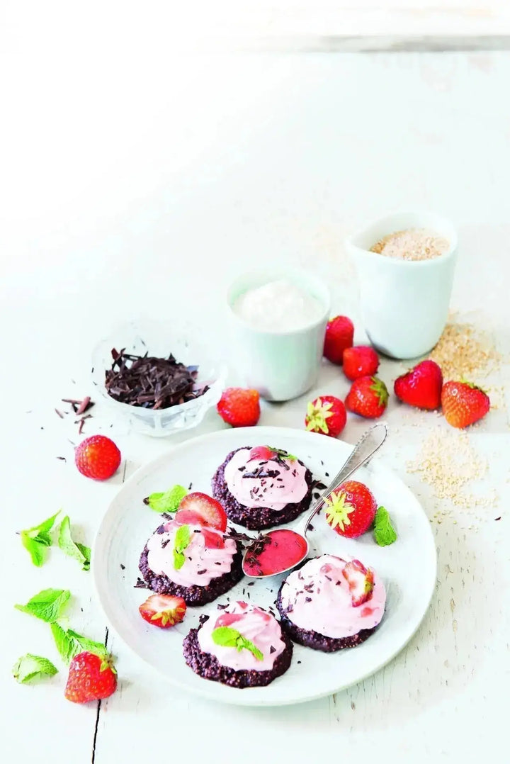 Schoko-Kokos-Taler mit Erdbeercreme auf einem weißen Teller, garniert mit frischen Erdbeeren, Kakaonibs und Minzblättern