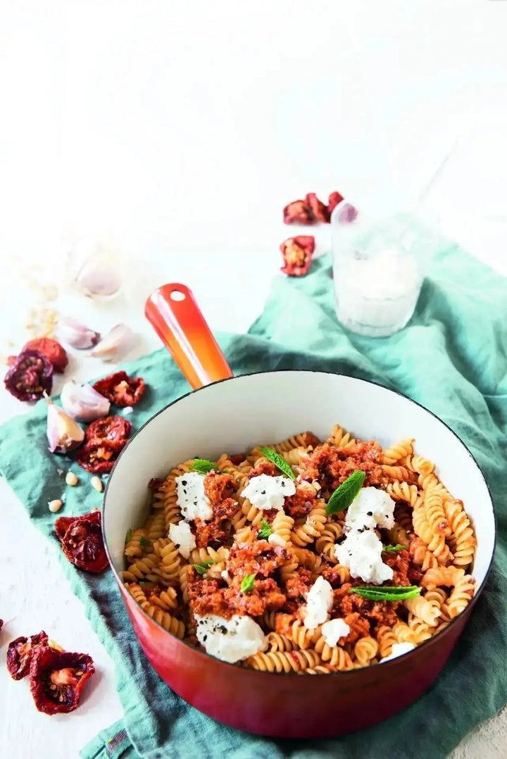 Spirelli-Nudeln mit Tomaten-Pesto und Ricotta, angerichtet auf einem Teller mit frischen Kräutern als Garnitur