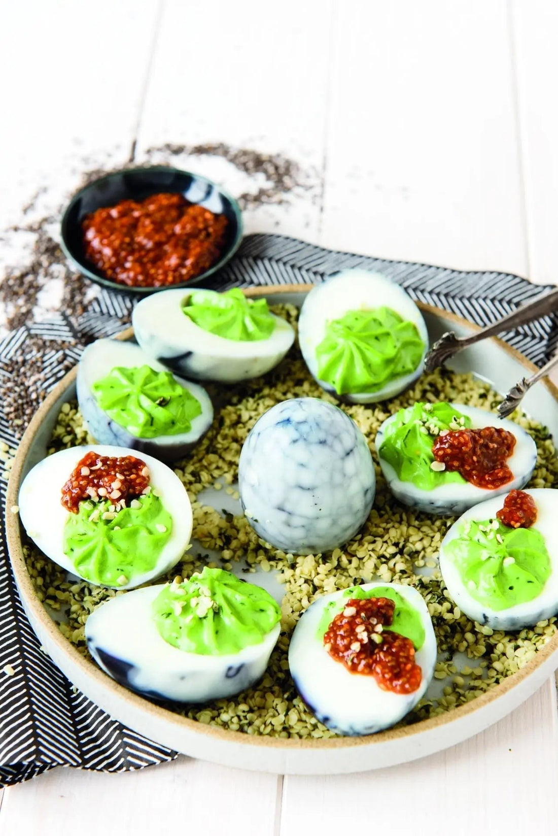 „Teufelseier mit Chili-Chia im grünen Hanfbett, angerichtet auf einem Keramikteller, farbenfroh und dekorativ serviert.