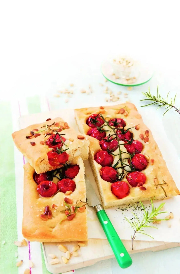 Tomaten-Focaccia mit Pinienkernen und Rosmarin, goldbraun gebacken und aufgeschnitten auf einem Holzbrett serviert