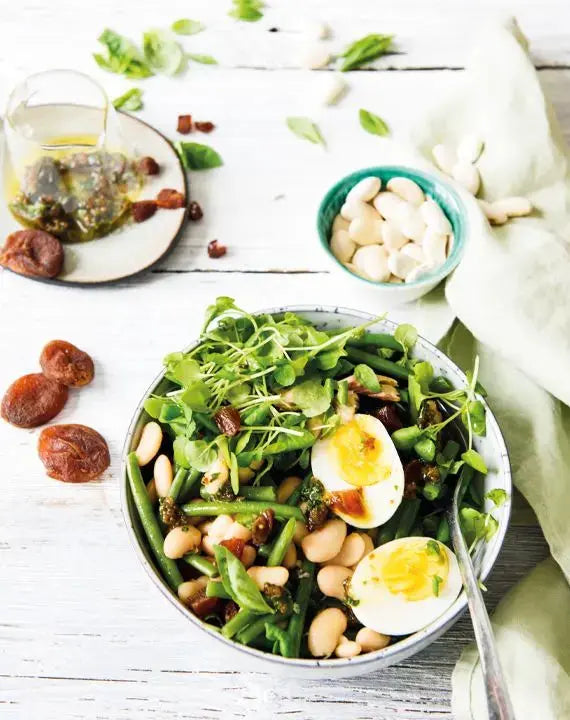 Weißer-Bohnen-Salat mit Basilikum-Aprikosen-Vinaigrette, farbenfroh angerichtet auf einem Teller mit frischen Kräutern