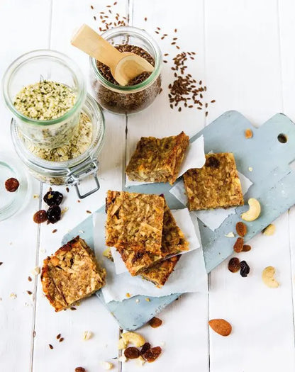 Premium-Müsli-Happen auf einem blauen Holzschneidebrett angerichtet, daneben Gläser mit Leinsamen und getrockneten Früchten.